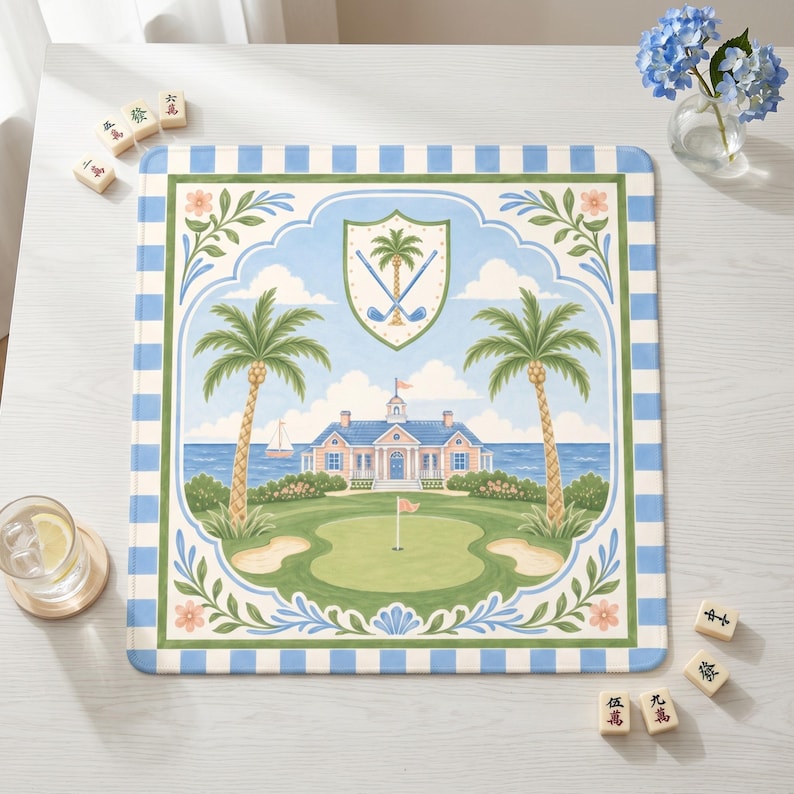 May include: Square golf-themed placemat with a blue and white striped border. The center features a golf course scene with palm trees, a clubhouse, and a shield emblem. The color palette includes shades of blue, green, and beige.