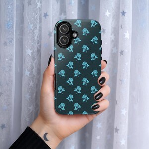 May include: A black smartphone case featuring a repeating pattern of light blue roses. The case has a textured appearance and a camera cutout. The phone case is held in a hand with black nail polish.