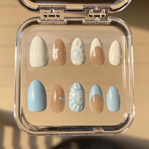 May include: A set of ten artificial nails in a clear plastic case. The nails feature a variety of designs, including solid white, light brown, and light blue. Some nails have a starfish or sun design.