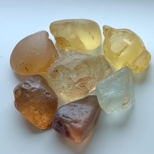 May include: A selection of smooth, rounded stones in shades of yellow, brown, and clear. The stones have a natural, irregular form and a slightly translucent quality, possibly gemstones or decorative rocks.