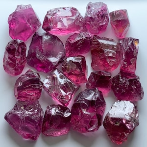 Puede incluir: Una colección de piedras preciosas en bruto, sin cortar, de varios tamaños y formas. Las piedras son de un color rosa intenso y vibrante, con una calidad translúcida. La textura rugosa de las piedras es visible.