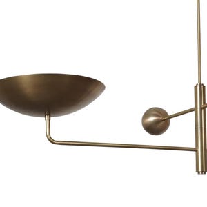May include: A modern brass-toned chandelier with a large, bowl-shaped shade and a spherical accent. The fixture has a minimalist design with straight lines and a warm metallic finish, suitable for interior lighting.