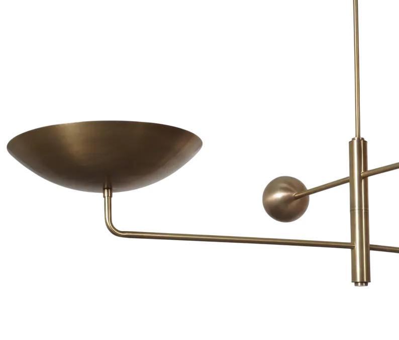 May include: A modern brass-toned chandelier with a large, bowl-shaped shade and a spherical accent. The fixture has a minimalist design with straight lines and a warm metallic finish, suitable for interior lighting.