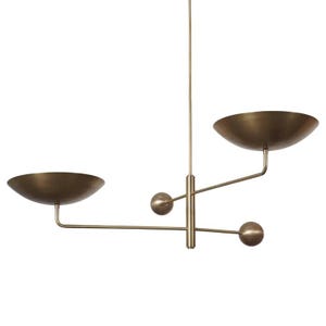 May include: A modern brass chandelier with two bowl-shaped shades and three spherical accents. The fixture hangs from a single rod, with the shades extending horizontally. The design is minimalist and elegant, suitable for various interior styles.