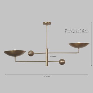 May include: A brass-toned chandelier with a modern design. The fixture has a 52-inch width and a 12-inch drop. It features two bowl-shaped shades and three spherical accents. The text in the image asks to confirm the total drop length.