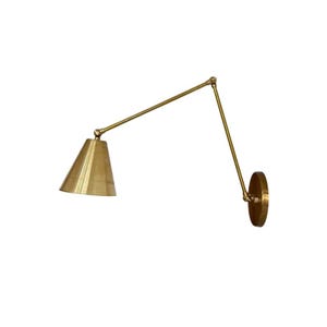 May include: A brass-colored wall-mounted lamp with a conical shade and an adjustable arm. The lamp has a circular base and a pivoting arm that allows for directional lighting. The design is minimalist and modern.
