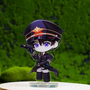 May include: A chibi-style acrylic figure of a character in a military-style uniform, holding two guns. The figure has a black hat with gold accents and a dark blue uniform. It stands on a clear base atop a wooden slice, with a green, mossy background.