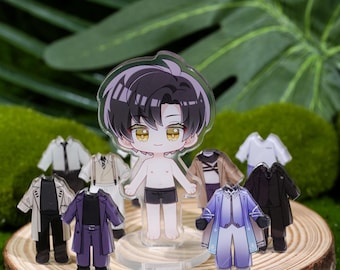 May include: A clear acrylic figure of a cartoon character with black hair and yellow eyes, surrounded by miniature outfits. The outfits include coats, shirts, and pants in various colors, displayed on a wooden slice.
