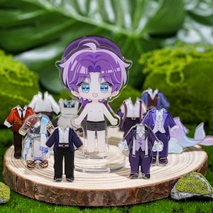 Peut inclure: Une figurine en acrylique transparente d'un personnage de dessin anim&eacute; aux cheveux violets et aux yeux bleus, entour&eacute;e de tenues miniatures. La figurine est pos&eacute;e sur une tranche de bois, avec un fond de mousse verte.