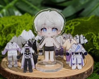 Puede incluir: Una figura acrílica transparente de un personaje de dibujos animados con cabello blanco y ojos azules, de pie sobre una base transparente. Pequeños trajes de varios colores y estilos rodean la figura, exhibidos sobre una rodaja de madera.