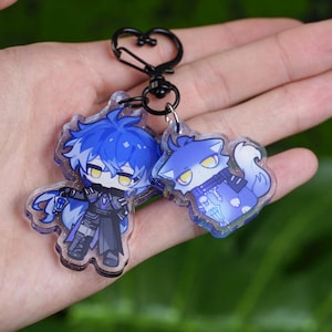 Puede incluir: Dos llaveros acrílicos con personajes de estilo anime. Un llavero representa un personaje con cabello azul y un atuendo oscuro. El otro llavero muestra un personaje azul con forma de lobo. Ambos están unidos a un llavero negro en forma de corazón.