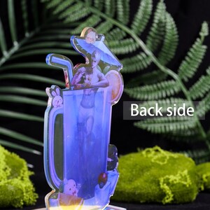 May include: A clear acrylic figure of a cocktail with a mermaid design. The drink has a blue hue, a straw, and a lemon slice. The words "Back side" are visible on the right side of the figure.