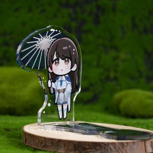 May include: A clear acrylic stand featuring a cartoon character with long brown hair, holding a parasol. The character is wearing a white and blue outfit. The stand is on a wooden base, set against a green, mossy background.