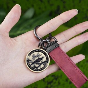 May include: A keychain with a claret leather strap and a round, gold-coloured pendant. The pendant features a bird design and the text "Destiny is in your own hands". The keychain has a metal ring and clasp.