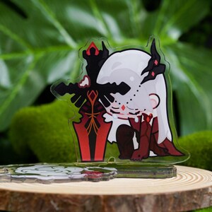 K&ouml;nnte beinhalten: Ein klarer Acryl-Charm mit einer Cartoonfigur mit wei&szlig;en Haaren, schwarzen Akzenten und roten Details, die ein rotes und schwarzes Schwert h&auml;lt. Der Charm wird auf einer Holzscheibe mit einem gr&uuml;nen, blattreichen Hintergrund pr&auml;sentiert.