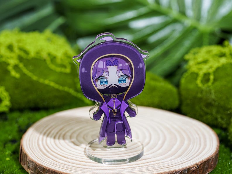 Peut inclure: Figurine acrylique violette de style anime repr&eacute;sentant un personnage avec une cape &agrave; capuche et un masque. La figurine a les yeux bleus et se tient sur une base transparente, plac&eacute;e sur une tranche de bois. Le fond pr&eacute;sente un feuillage vert.