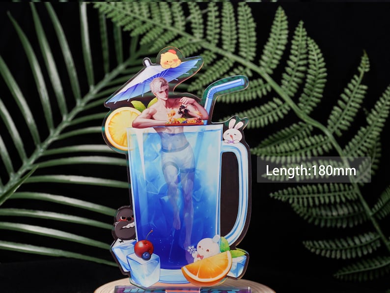 May include: A colorful acrylic standee featuring a man in a blue drink with a straw. The standee has a length of 180mm. It includes a lemon slice, ice cubes, and cartoon characters like a bunny and a bird. The background is a fern.