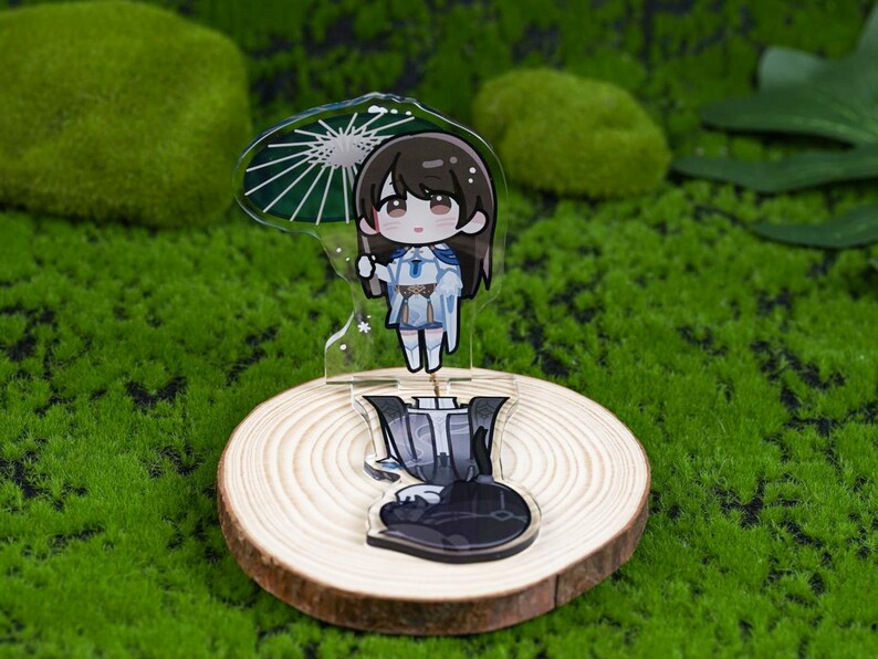 May include: A clear acrylic anime-style figure of a character holding an umbrella. The figure is on a wooden slice base. The character has brown hair and is wearing a blue and white outfit. The umbrella is green and white. The background is green.