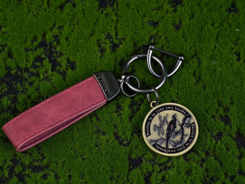 May include: A burgundy leather keychain with a metal clasp and a round pendant. The pendant features a bird design and the text "Destiny is in your own hands."