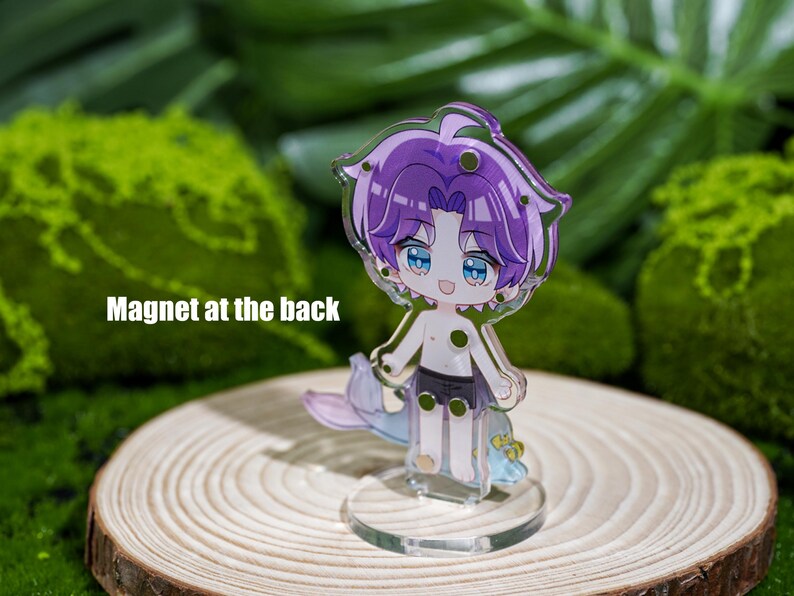 Peut inclure: Un charm en acrylique transparent repr&eacute;sentant un personnage de dessin anim&eacute; aux cheveux violets et aux yeux bleus. Le personnage est torse nu, porte un short noir et a une queue de sir&egrave;ne. Le charm est sur un support transparent. Le texte "Magnet at the back" est visible.