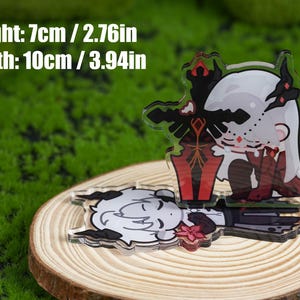 K&ouml;nnte beinhalten: Zwei Acryl-Anh&auml;nger mit Anime-Charakteren, einer stehend und einer liegend. Der stehende Anh&auml;nger hat ein schwarzes Schwert und rote Akzente. Die Anh&auml;nger sind 7 cm hoch und 10 cm breit. Sie liegen auf einer Holzscheibe.