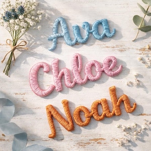 Może przedstawiać: Haftowane imiona Ava, Chloe i Noah w niebieskiej, różowej i pomarańczowej nici. Imiona są w kursywie. Obraz zawiera również bukiet kwiatów i niebieską wstążkę na białej drewnianej powierzchni.