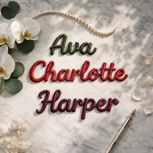 Può includere: Toppe con nomi ricamati in verde, rosso e bordeaux: "Ava", "Charlotte" e "Harper". I nomi sono visualizzati su una superficie di marmo, con una collana di perle, fiori e una penna.