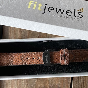 May include: A brown snakeskin-effect watch strap is presented in a white box, with the gold text "fit jewels by francisco". The leather strap has a black buckle and is displayed on a black surface.