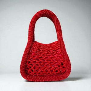 May include: A small, red crocheted handbag with a rounded shape and a single handle. The bag features an open, lacy design on the front, revealing a red lining. The handle and edges are tightly crocheted.