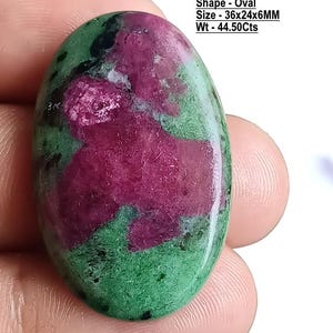 Op de afbeelding: Een ovaalvormige natuurlijke robijn-zoisiet edelsteen met een gepolijst oppervlak. De steen vertoont een mix van levendig magentarood en diepgroen met zwarte insluitingen. Tekst: Stone - Natural Ruby Zoisite, Shape - Oval, Size - 36x24x6MM, Wt - 44.50Cts.
