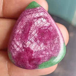 May include: A teardrop-shaped gemstone, polished to a high sheen. The stone is predominantly magenta, with a complex pattern of fine lines. The top edge is a vivid green, providing a strong colour contrast.