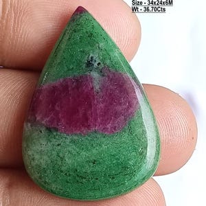 Op de afbeelding: Een peervormige natuurlijke robijn zoisiet edelsteen met een glad, gepolijst oppervlak. De steen heeft een levendige groene basis met opvallende diep magenta insluitingen. De tekst op de afbeelding luidt: Stone - Natural Ruby Zoisite, Shape - Pear, Size - 34x24x6M, Wt - 36.70Cts.