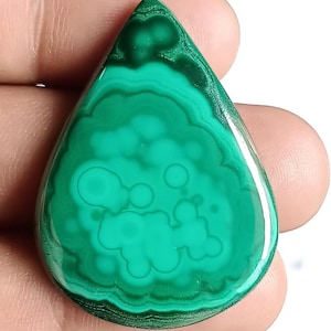 May include: A polished, teardrop-shaped malachite gemstone. The stone displays concentric bands of varying shades of green, creating a swirling pattern. The surface is smooth and glossy, with a high degree of polish, highlighting the natural patterns.