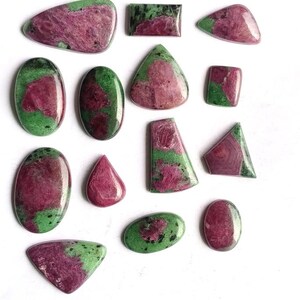 Puede incluir: Una colección de trece piedras preciosas de rubí en zoisita pulidas en varias formas, incluyendo óvalos, triángulos y rectángulos. Cada piedra presenta un patrón moteado distintivo de inclusiones de rubí magenta intenso dentro de una matriz de zoisita verde.