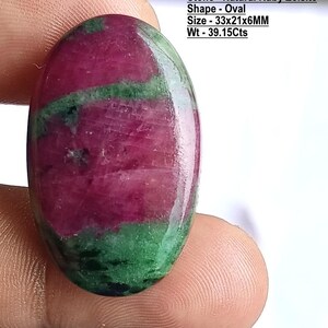 Op de afbeelding: Een ovaalvormige natuurlijke robijn zoisiet edelsteen met een gepolijst oppervlak. De steen heeft een mix van diep magenta en donkergroene kleuren. De tekst op de afbeelding luidt: Stone - Natural Ruby Zoisite, Shape - Oval, Size - 33x21x6MM, Wt - 39.15Cts.