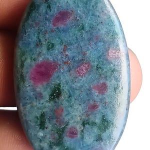May include: Oval gemstone with a polished surface. The stone displays a mix of blue-green shades with scattered patches of deep pink and red. The overall appearance is smooth and natural, showcasing the stone's unique colour variations.