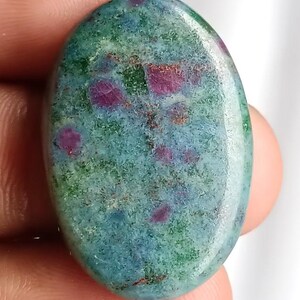 Op de afbeelding: Ovale edelsteen met een gevlekt uiterlijk. De steen heeft tinten van blauwgroen, groen en rood. Rode insluitsels zijn verspreid, waardoor een uniek patroon ontstaat. De gepolijste steen is glad. Ideaal voor sieraden.