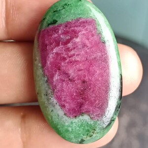 Può includere: Pietra preziosa ovale con una vibrante combinazione di colori. Il centro è di un rosa-rosso intenso, circondato da un bordo verde con inclusioni scure. La superficie lucida riflette la luce, evidenziando i motivi naturali.