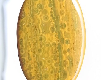 May include: Polished, oval gemstone displaying a pattern of yellow and green tones. The stone's surface features circular and linear patterns. The gemstone is held between two fingers.