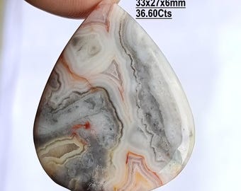 May include: A pear-shaped Yellow Crazy Lace Agate gemstone featuring intricate swirling patterns in shades of white, gray, and soft orange. The stone measures 33x27x6mm and weighs 36.60cts, with text printed on the image detailing these specifications.