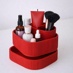 May include: A red, tiered organizer filled with beauty products. The organizer has a ribbed texture and holds bottles, tubes, and makeup brushes. The items are arranged in separate compartments, creating a neat and organized display.