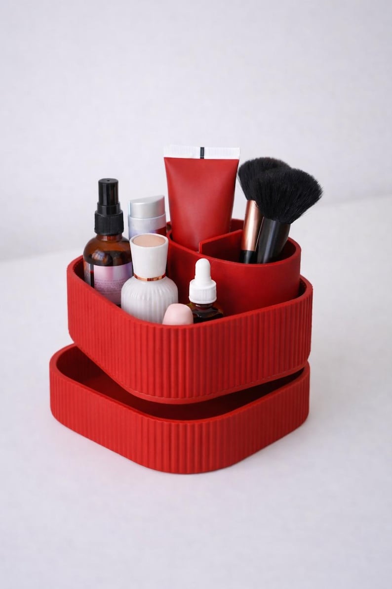 Puede incluir: Un organizador rojo de varios niveles lleno de productos de belleza. El organizador tiene una textura acanalada y contiene botellas, tubos y brochas de maquillaje. Los art&iacute;culos est&aacute;n dispuestos en compartimentos separados.