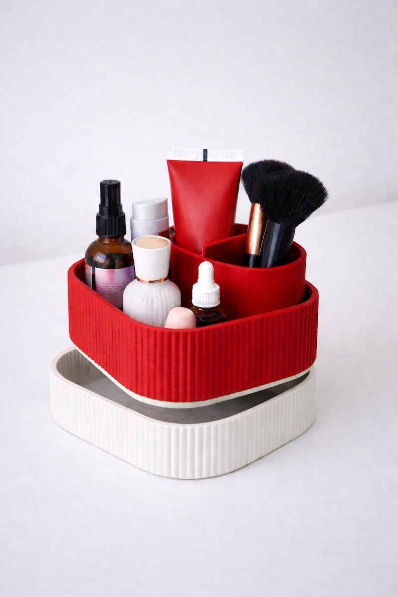 Puede incluir: Un organizador rojo y blanco de dos niveles lleno de productos de belleza. El nivel superior es rojo y contiene brochas de maquillaje, un tubo rojo y varias botellas. El nivel inferior es blanco. El organizador est&aacute; dise&ntilde;ado para guardar cosm&eacute;ticos y productos para el cuidado de la piel.
