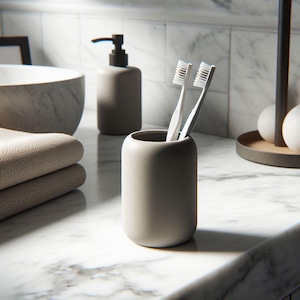 Può includere: Una scena di bagno moderno con un portaspazzolini grigio con due spazzolini bianchi. Sono visibili anche un dosatore di sapone abbinato e asciugamani piegati. Gli oggetti sono disposti su un piano di lavoro in marmo.