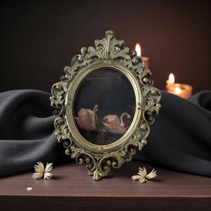 May include: An antique oval picture frame with an ornate gold finish. The frame holds a painting of two swans on a dark background. The frame is set on a wooden surface with a dark grey cloth and candles in the background.