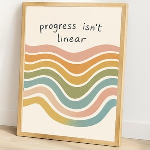 May include: A framed art print with the text "progress isn't linear" above a series of colorful, wavy stripes. The stripes include shades of pink, orange, yellow, green, and blue. The frame is made of light-colored wood.
