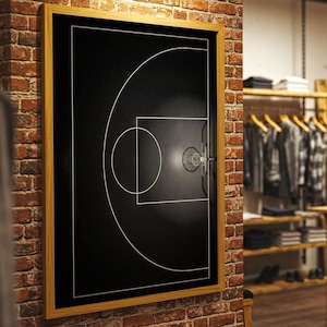 Könnte beinhalten: Ein gerahmtes schwarz-weißes Basketballfeld-Diagramm hängt an einer Backsteinmauer in einem Bekleidungsgeschäft. Das Geschäft verfügt über Holztische und Kleiderständer.