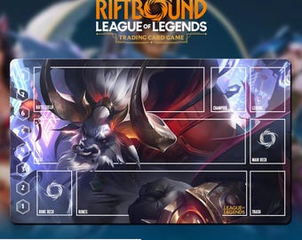May include: A rectangular playmat for the League of Legends trading card game. The mat features a detailed illustration of a character with large horns and a fierce expression. The mat has designated zones for cards and the text "RIFTBOUND LEAGUE OF LEGENDS TRADING CARD GAME".