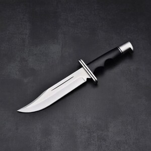 May include: A stainless steel hunting knife with a black handle and a silver bolster. The blade is sharp and curved, with a single fuller. The knife is designed for outdoor use and survival.