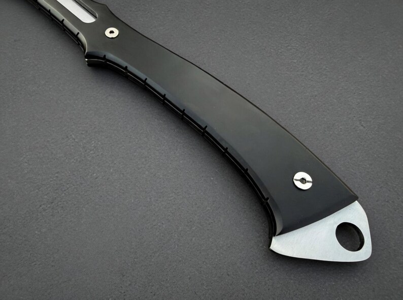 May include: Close-up of a black knife handle with a silver blade. The handle is curved and has a smooth, glossy finish. The blade has a hole near the end. The knife appears to be a folding knife.